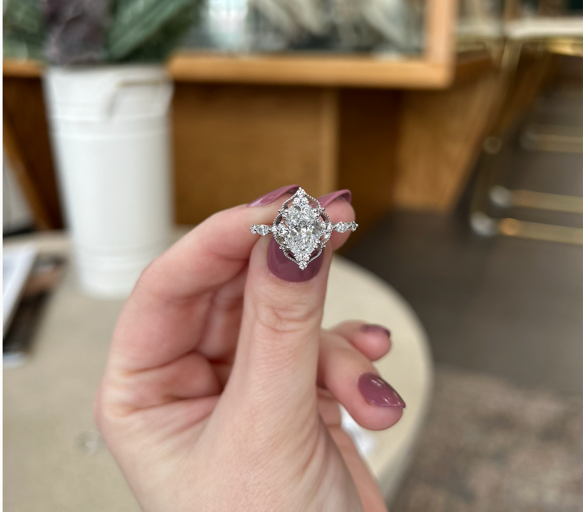 Ornate oval diamond engagement ring in white metal, held in a jewelry showroom